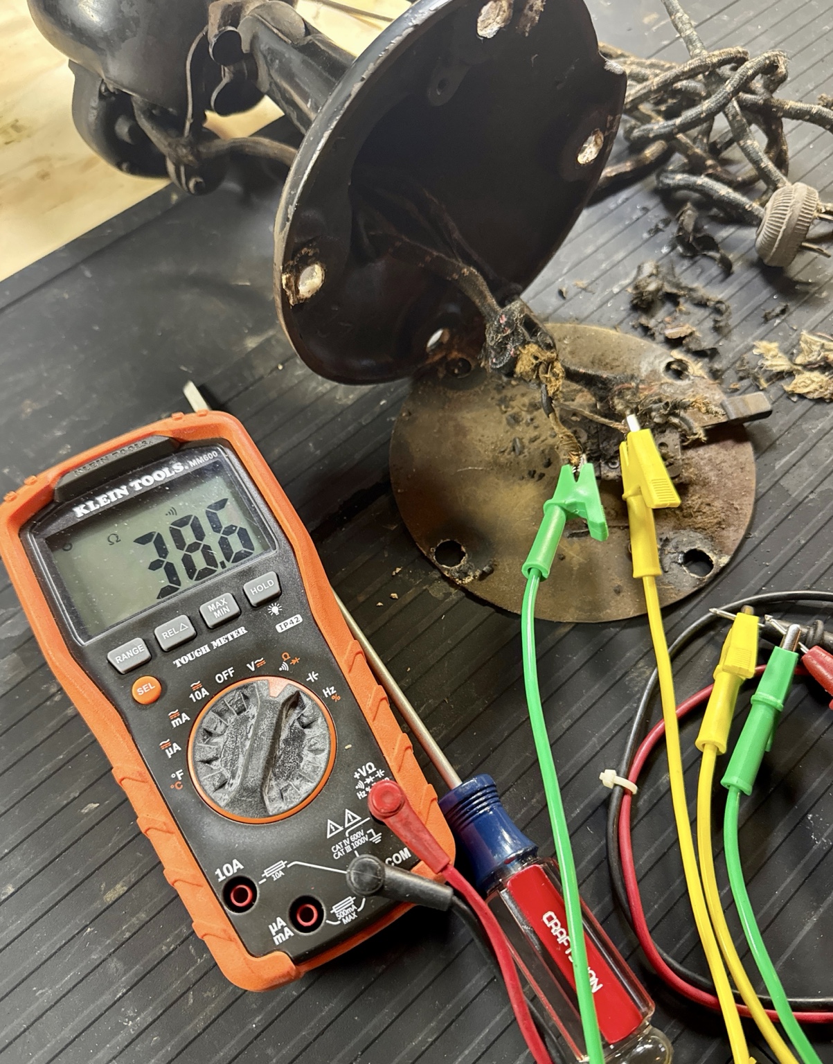 Antique fan being tested on a workbench beside vintage meters and warm Edison bulbs.