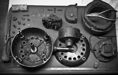 Top-down view of a vintage workbench showing an antique fan completely disassembled for restoration.