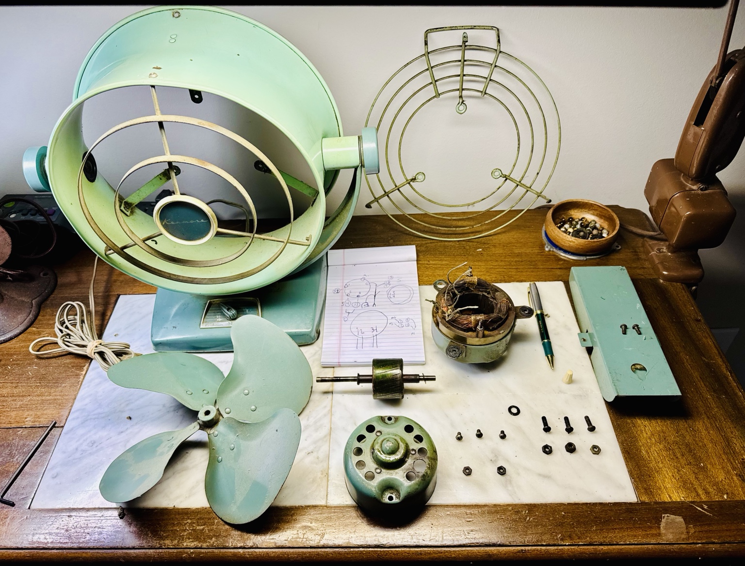 Overhead view of antique fan parts and tools arranged on a workbench.